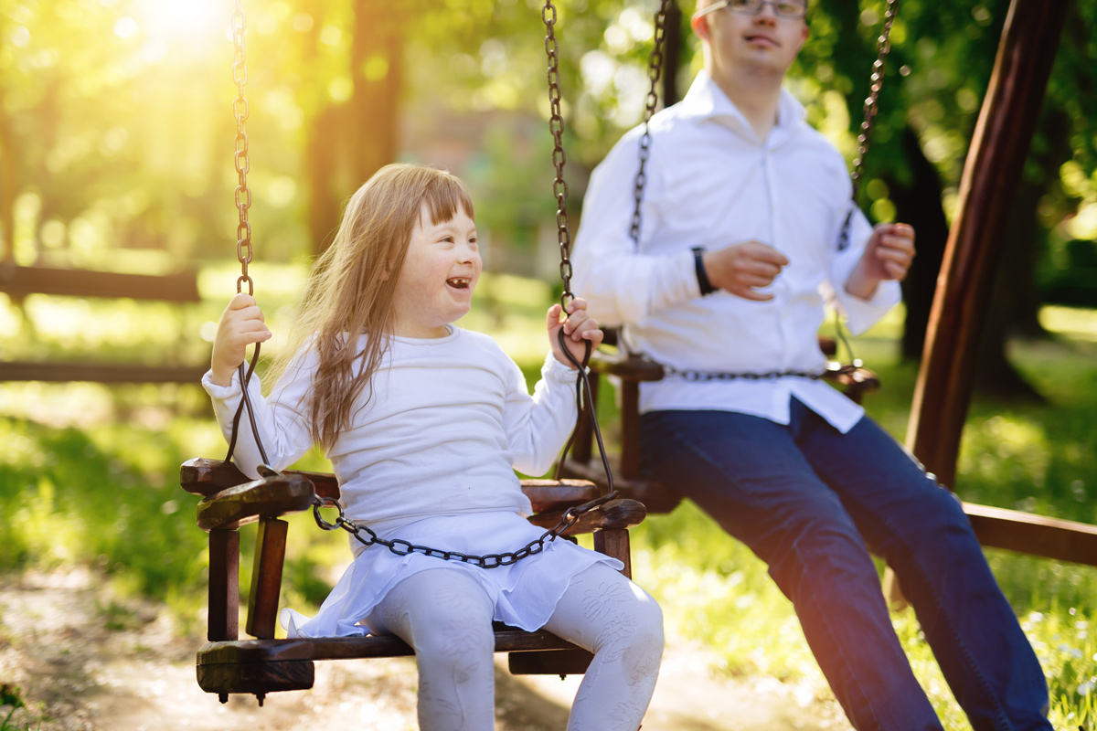 En skrattande flicka och en pojke gungar sida vid sida i solnedgången.